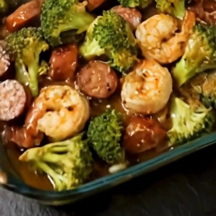 A glass baking dish filled with roasted pink shrimp, caramelized smoked sausage coins
