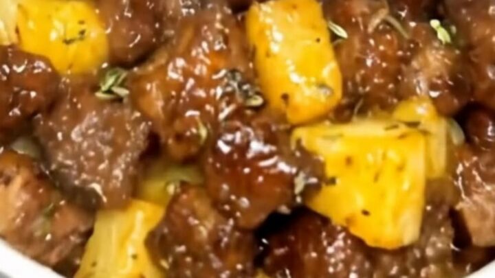 A white ceramic bowl filled with glistening, seared steak cubes and caramelized pineapple chunks coated in a sticky glaze