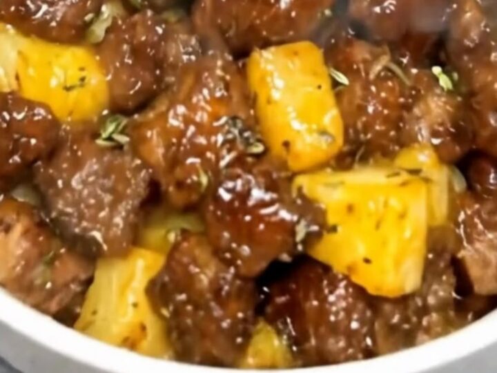 A white ceramic bowl filled with glistening, seared steak cubes and caramelized pineapple chunks coated in a sticky glaze