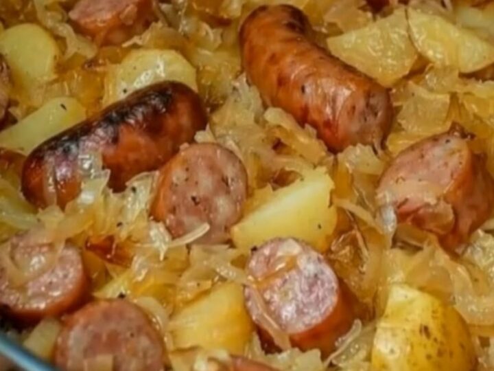 A black cast iron skillet filled with browned Polish sausage slices, golden potatoes, and steaming sauerkraut.