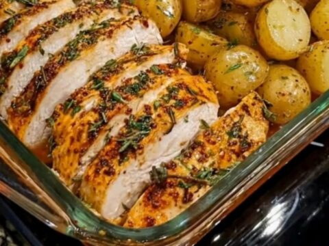 A glass baking dish containing sliced seasoned chicken breast, roasted baby potatoes, and tender green beans.