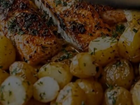 A glass baking dish containing succulent herb-crusted salmon fillets, golden roasted baby potatoes, and tender asparagus.