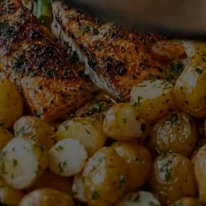 A glass baking dish containing succulent herb-crusted salmon fillets, golden roasted baby potatoes, and tender asparagus.