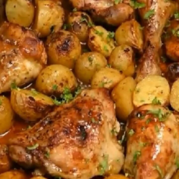 A deep metal pan filled with glistening, golden-brown honey garlic chicken drumsticks and roasted baby potatoes