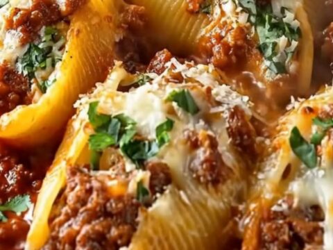 A hot skillet of beef stuffed shells with a fork lifting a cheese-pulling shell dripping with meat sauce