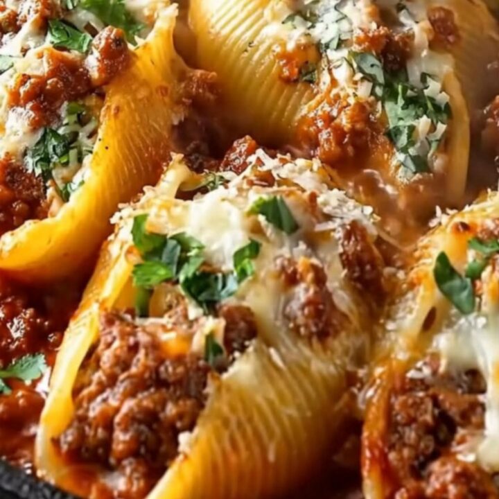 A hot skillet of beef stuffed shells with a fork lifting a cheese-pulling shell dripping with meat sauce
