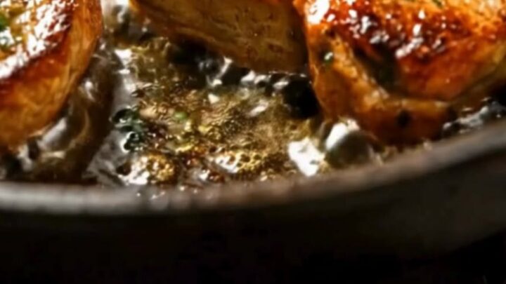 Four golden seared pork chops in a cast-iron skillet, topped with melting dollops of garlic butter and fresh parsley.