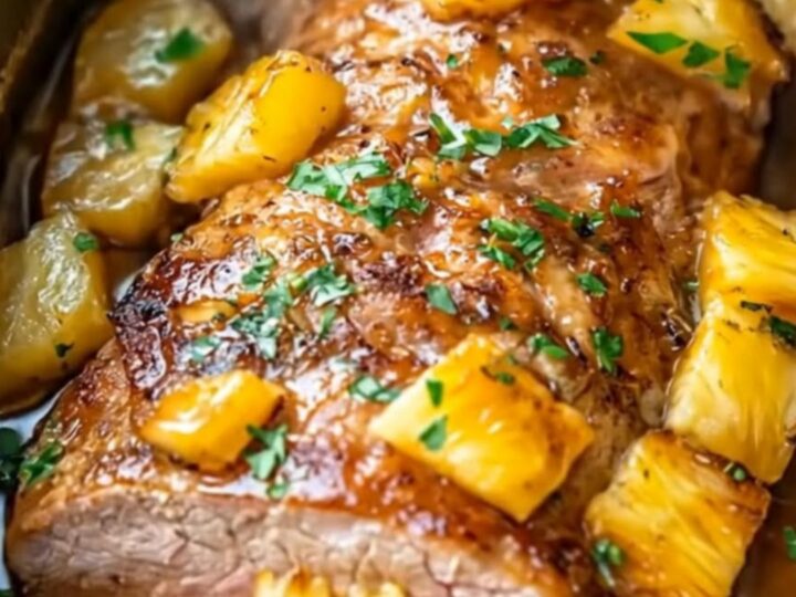 A beautifully glazed, sliced pineapple pork roast served in an oval slow cooker surrounded by caramelized pineapple cubes.