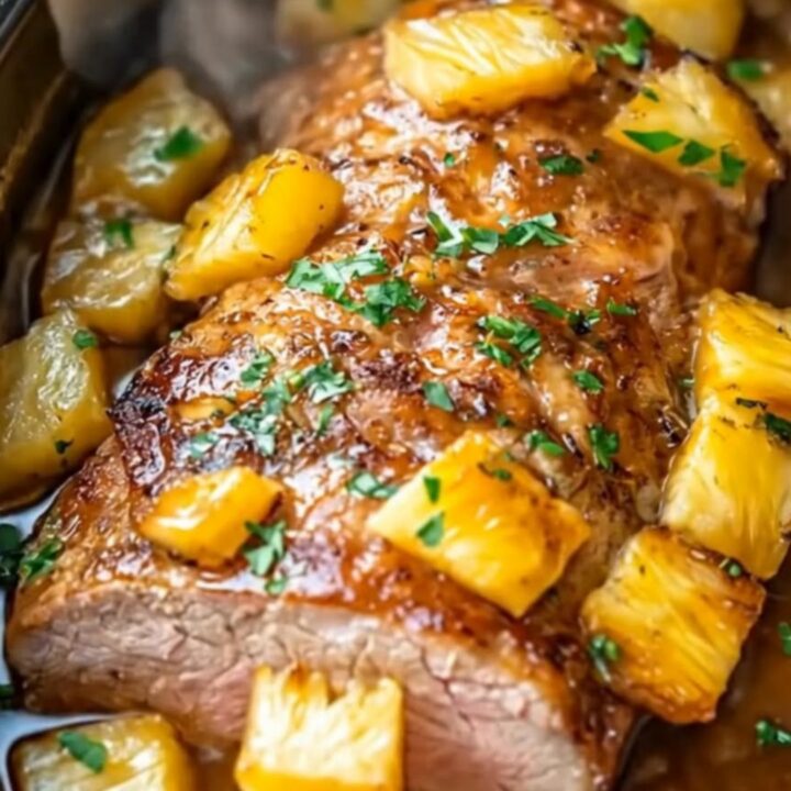 A beautifully glazed, sliced pineapple pork roast served in an oval slow cooker surrounded by caramelized pineapple cubes.