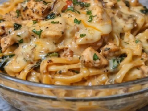 A steaming bowl of glossy creamy chicken linguine with visible spinach, onions, and melted cheese strings