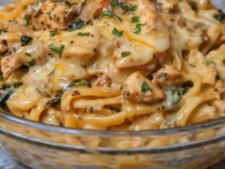 A steaming bowl of glossy creamy chicken linguine with visible spinach, onions, and melted cheese strings