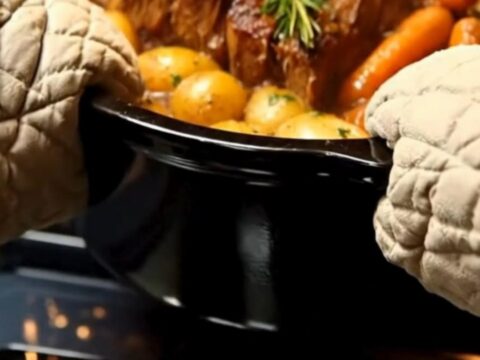 A hot black roasting pot filled with tender, steaming pot roast, whole baby potatoes, and carrots.
