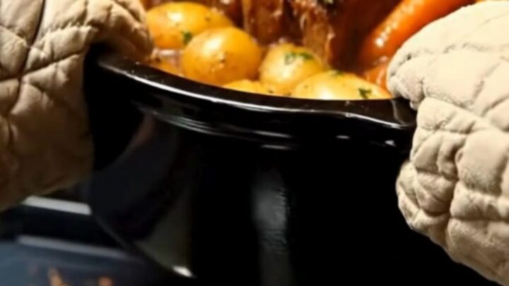 A hot black roasting pot filled with tender, steaming pot roast, whole baby potatoes, and carrots.