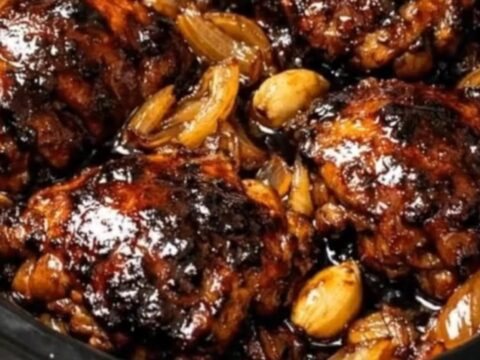 Tender, caramelized glazed chicken thighs resting with onions and garlic in a black slow cooker