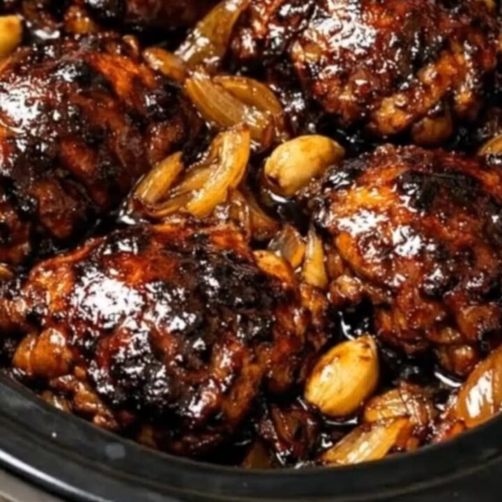 Tender, caramelized glazed chicken thighs resting with onions and garlic in a black slow cooker