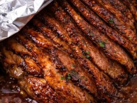 A beautifully glazed spiral-sliced ham resting in its bubbling brown sugar mustard juices inside a metal roasting pan.