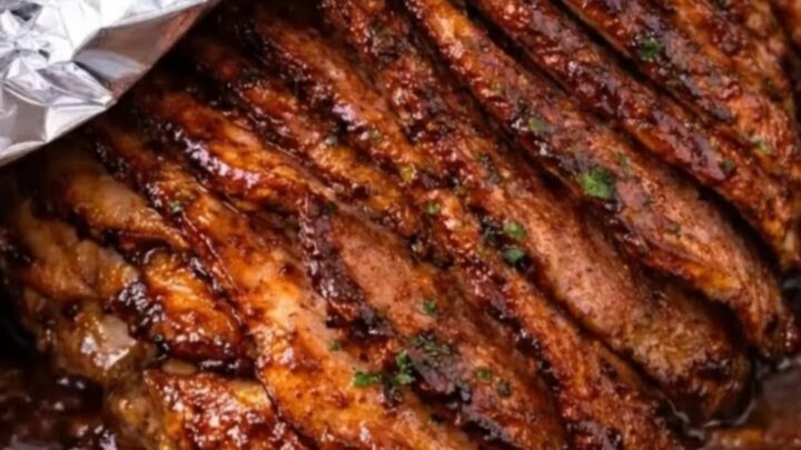 A beautifully glazed spiral-sliced ham resting in its bubbling brown sugar mustard juices inside a metal roasting pan.