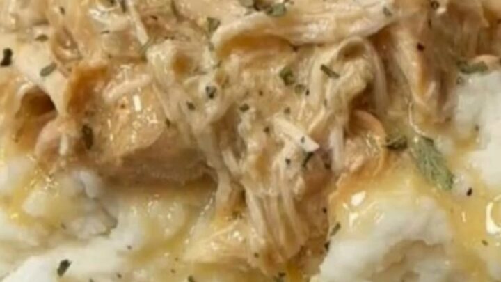 Thick savory golden chicken gravy pouring from a ladle over tender shredded chicken and fluffy mashed potatoes