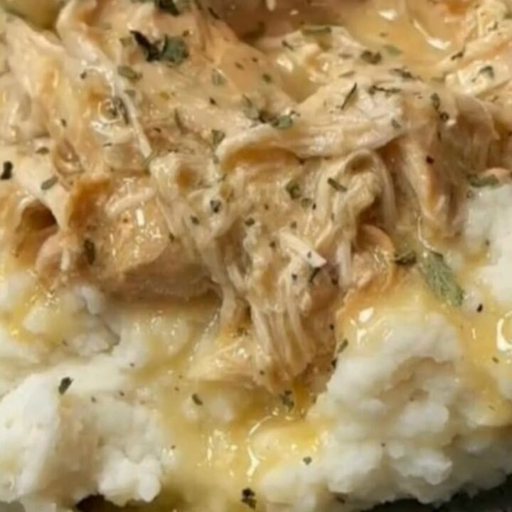 Thick savory golden chicken gravy pouring from a ladle over tender shredded chicken and fluffy mashed potatoes
