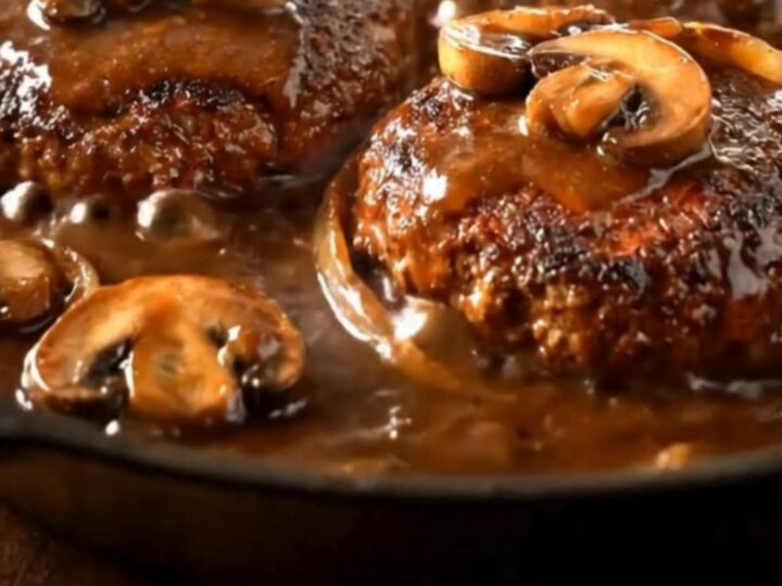 A rustic cast-iron skillet containing juicy seared hamburger steaks smothered in a rich