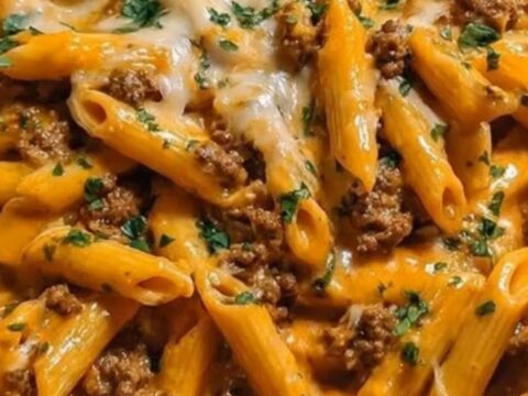 A stainless steel skillet filled with creamy orange penne pasta, browned ground beef, melted cheddar cheese