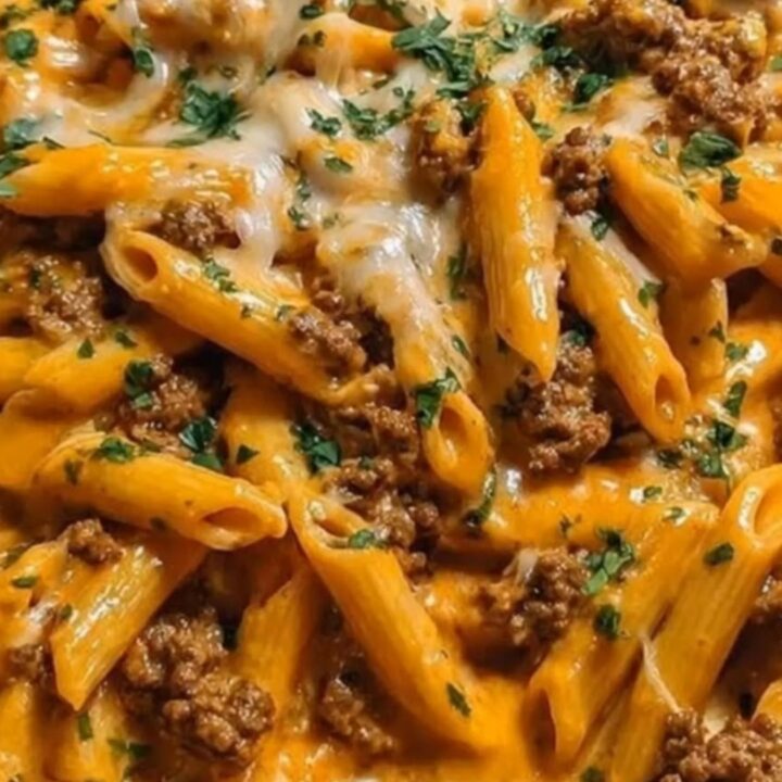 A stainless steel skillet filled with creamy orange penne pasta, browned ground beef, melted cheddar cheese