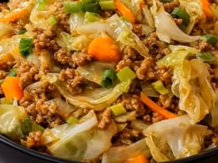 A large black bowl filled with steaming savory beef and cabbage stir fry, garnished with sliced green onions