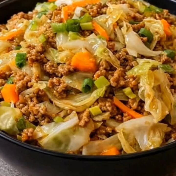 A large black bowl filled with steaming savory beef and cabbage stir fry, garnished with sliced green onions