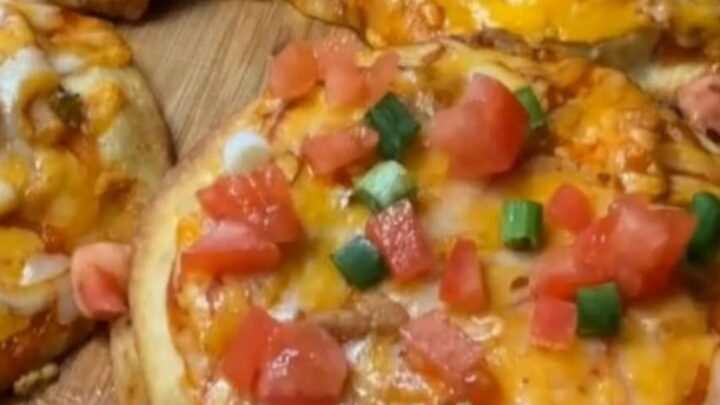 A wooden board holding crispy mini chicken Mexican pizzas with bubbly melted cheese and fresh scallions.
