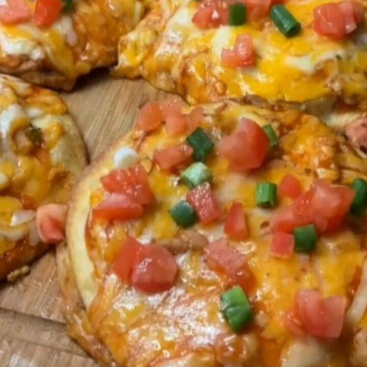 A wooden board holding crispy mini chicken Mexican pizzas with bubbly melted cheese and fresh scallions.
