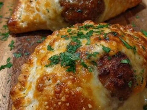 Four golden-brown, flaky puff pastry pockets lined up on a rustic wooden serving board with parsley sprinkles.