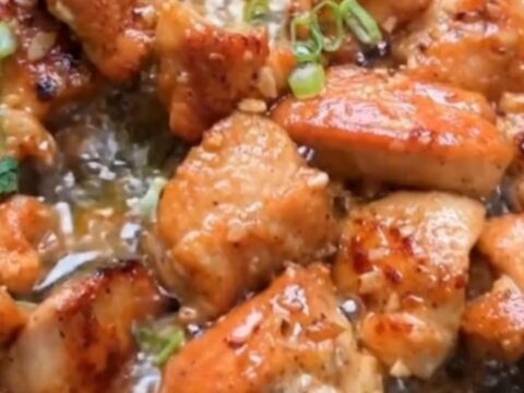 A skillet filled with golden-brown, seared chicken bites glistening in foaming garlic butter and garnished with fresh green