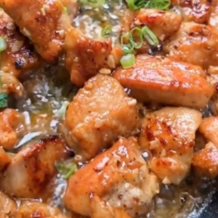 A skillet filled with golden-brown, seared chicken bites glistening in foaming garlic butter and garnished with fresh green