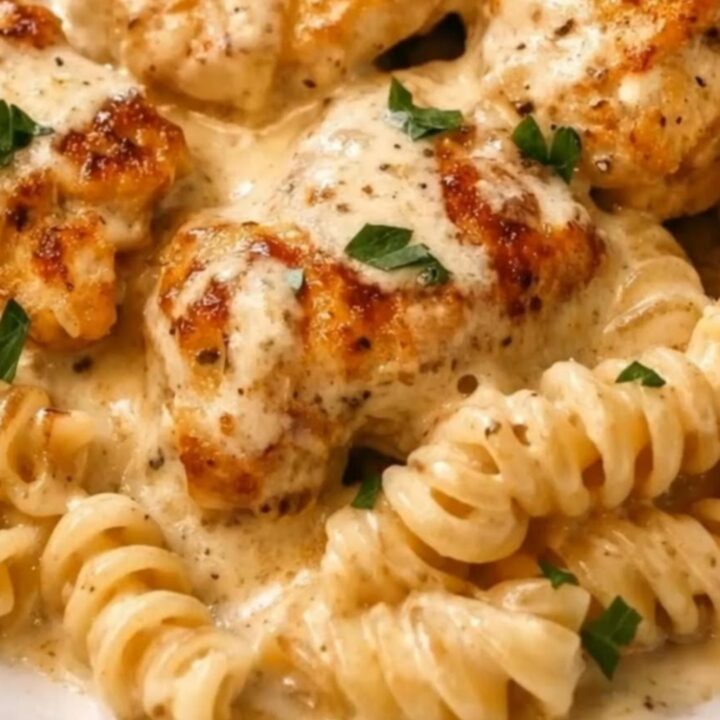 A fork twirling glossy rotini pasta drenched in a velvety garlic parmesan cream sauce next to seared chicken.