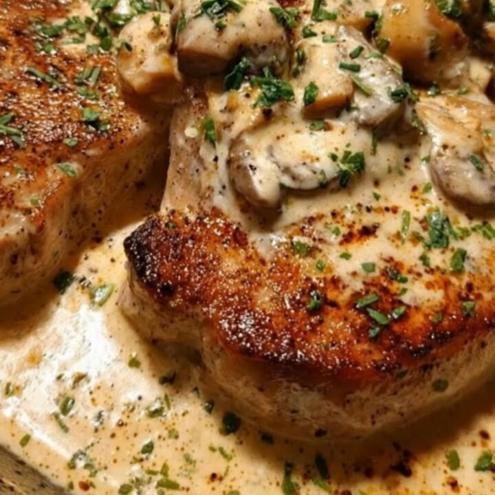 A seared pork chop smothered in a thick mushroom cream sauce and garnished with fresh parsley in a dark skillet