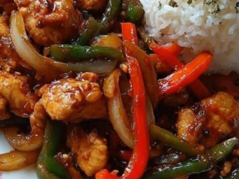A patterned plate showcasing glossy sweet and spicy chicken stir-fry next to golden potato wedges and white rice.