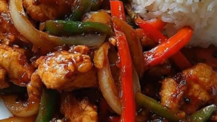 A patterned plate showcasing glossy sweet and spicy chicken stir-fry next to golden potato wedges and white rice.