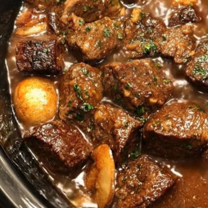 A black oval crock pot filled with glossy slow-cooked beef tips and tender mushrooms in rich brown gravy.