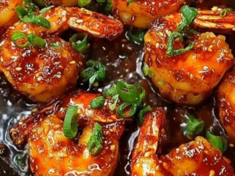 A cast-iron skillet filled with glossy, caramelized honey garlic shrimp garnished with sliced green onions.