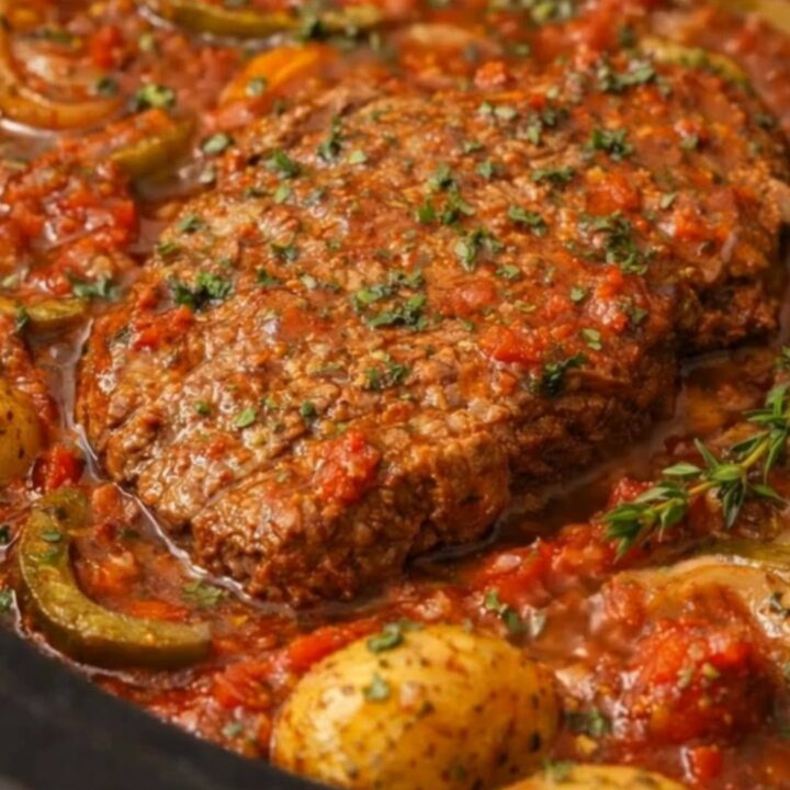Tender Swiss steak portion served inside a black slow cooker surrounded by green peppers and baby yellow potatoes