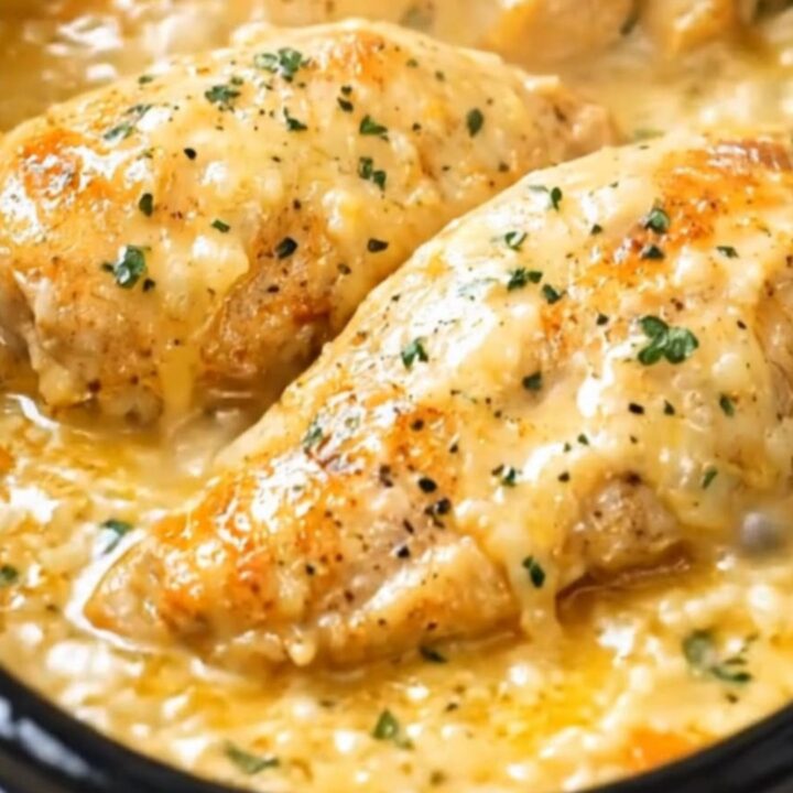Tender chicken breasts resting in a thick, glossy parmesan cheese sauce inside a black slow cooker