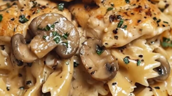A white bowl filled with creamy farfalle pasta, seared chicken pieces, and sautéed mushrooms with steam rising.