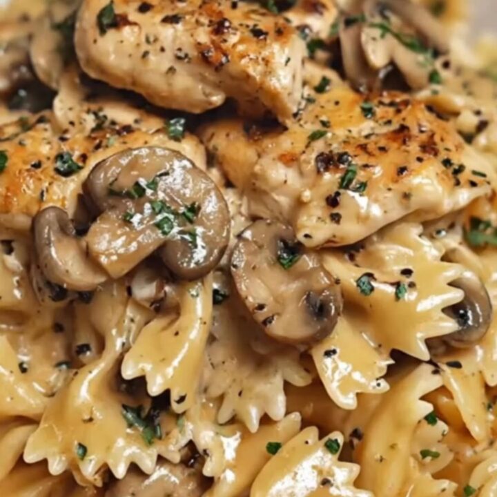 A white bowl filled with creamy farfalle pasta, seared chicken pieces, and sautéed mushrooms with steam rising.