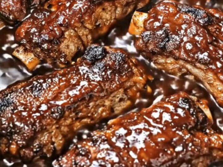 A close-up of tender, glazed country-style pork ribs glistening with thick, dark barbecue sauce inside a slow cooker.