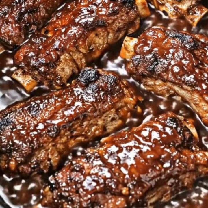 A close-up of tender, glazed country-style pork ribs glistening with thick, dark barbecue sauce inside a slow cooker.