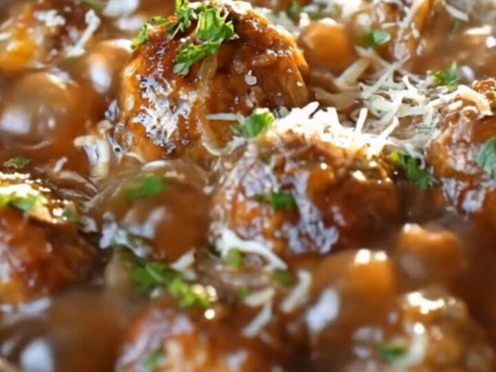 Slow cooker French onion meatballs simmering in rich glossy gravy topped with melted cheese and fresh parsley