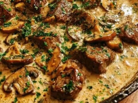 A rustic cast iron skillet filled with creamy beef and mushroom gravy, garnished with fresh chopped parsley.