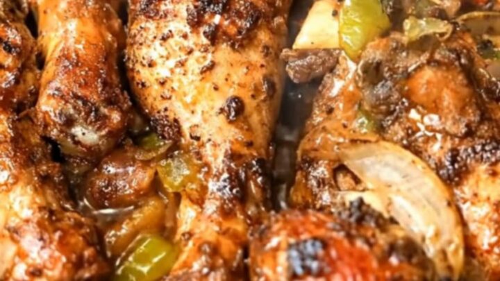 A black rectangular roasting pan filled with glossy, caramelized honey garlic chicken drumsticks over roasted peppers.