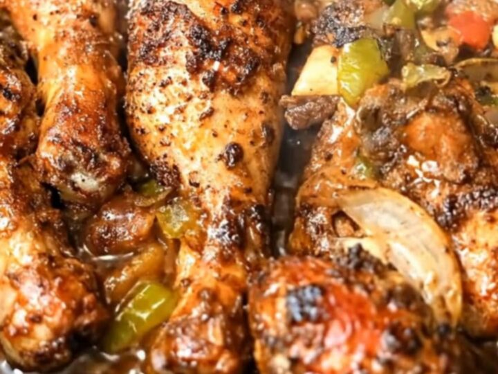 A black rectangular roasting pan filled with glossy, caramelized honey garlic chicken drumsticks over roasted peppers.