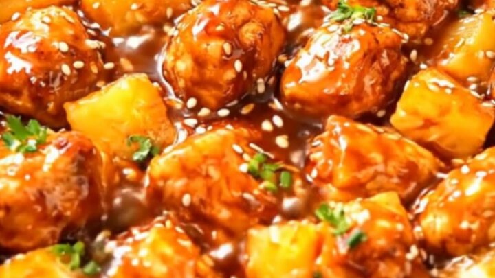 A black slow cooker filled with glistening, tender chicken pieces and pineapple chunks coated in a sticky glaze